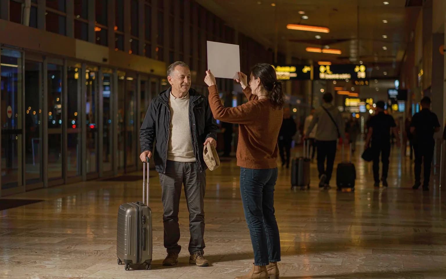 A hospital arrival coordinator holding a name board for an international patient at an airport arrivals hall