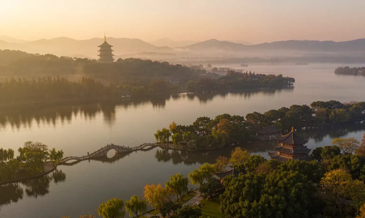 West Lake in Hangzhou at dusk with its arched bridge, pavilions and misty hills